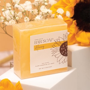 May include: A bar of honey-scented soap with a sunflower graphic on the label. The label reads "HAND-MADE BAR SOAP Honey 100% ORGANIC PLANT ESSENTIAL OIL SOAP NET WT 3.5OZ/100G".