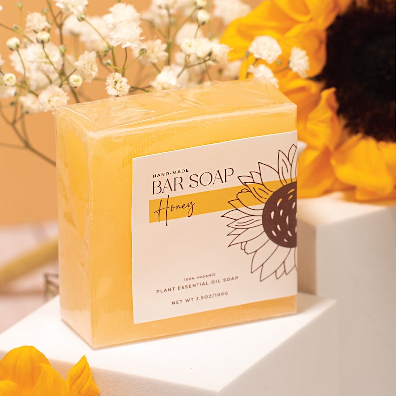 May include: A bar of honey-scented soap with a sunflower graphic on the label. The label reads "HAND-MADE BAR SOAP Honey 100% ORGANIC PLANT ESSENTIAL OIL SOAP NET WT 3.5OZ/100G".