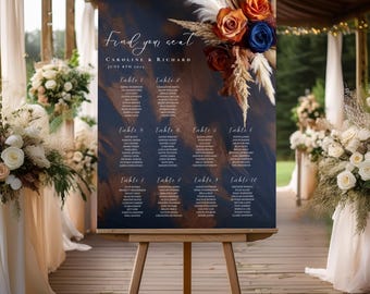 May include: A navy blue wedding seating chart with gold accents and a floral arrangement of dried grasses, orange and blue flowers. The chart lists guest names and table numbers for Caroline and Richard's wedding on June 8th, 2014.