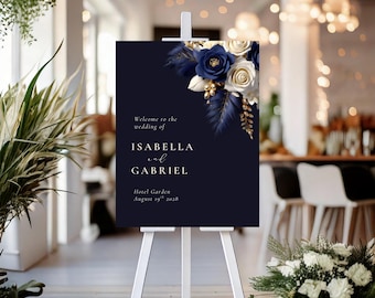 May include: A navy blue wedding welcome sign on a white easel. The sign features floral accents in white, gold, and navy blue. Text on the sign reads "Welcome to the wedding of ISABELLA and GABRIEL" and event details.