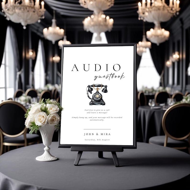 May include: A black sign with white text that reads "AUDIO guestbook". A black rotary phone with gold accents is illustrated on the sign. The text below the phone reads "Feel free to give us a call and leave a message! Simply hang up, and your message will be recorded automatically." The sign also includes the names "JOHN & MIRA" and the date "Saturday, 8th August".