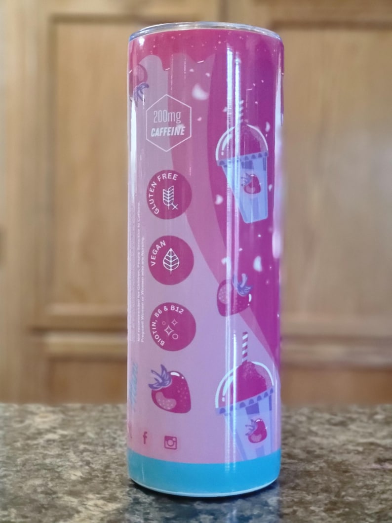 May include: A cylindrical tumbler with a pink and purple strawberry design. The tumbler features the text "200mg Caffeine", and icons indicating it is gluten-free and vegan. The bottom of the tumbler is light blue.