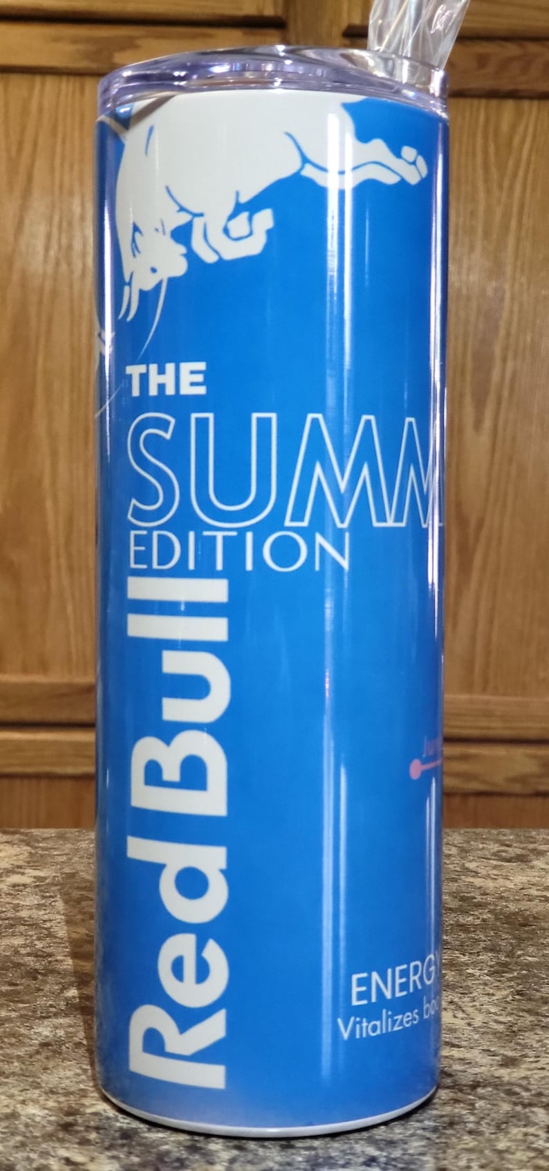 Może przedstawiać: Błękitna i biała puszka napoju energetycznego Red Bull z białym logo byka i tekstem "The Summer Edition".