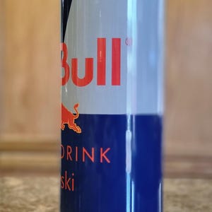 Pu&ograve; includere: Un bicchiere in acciaio inossidabile con un design Red Bull blu e bianco. Il bicchiere ha un coperchio trasparente e una cannuccia. Il testo sul bicchiere recita "Red Bull" e "Drink Your Wings".