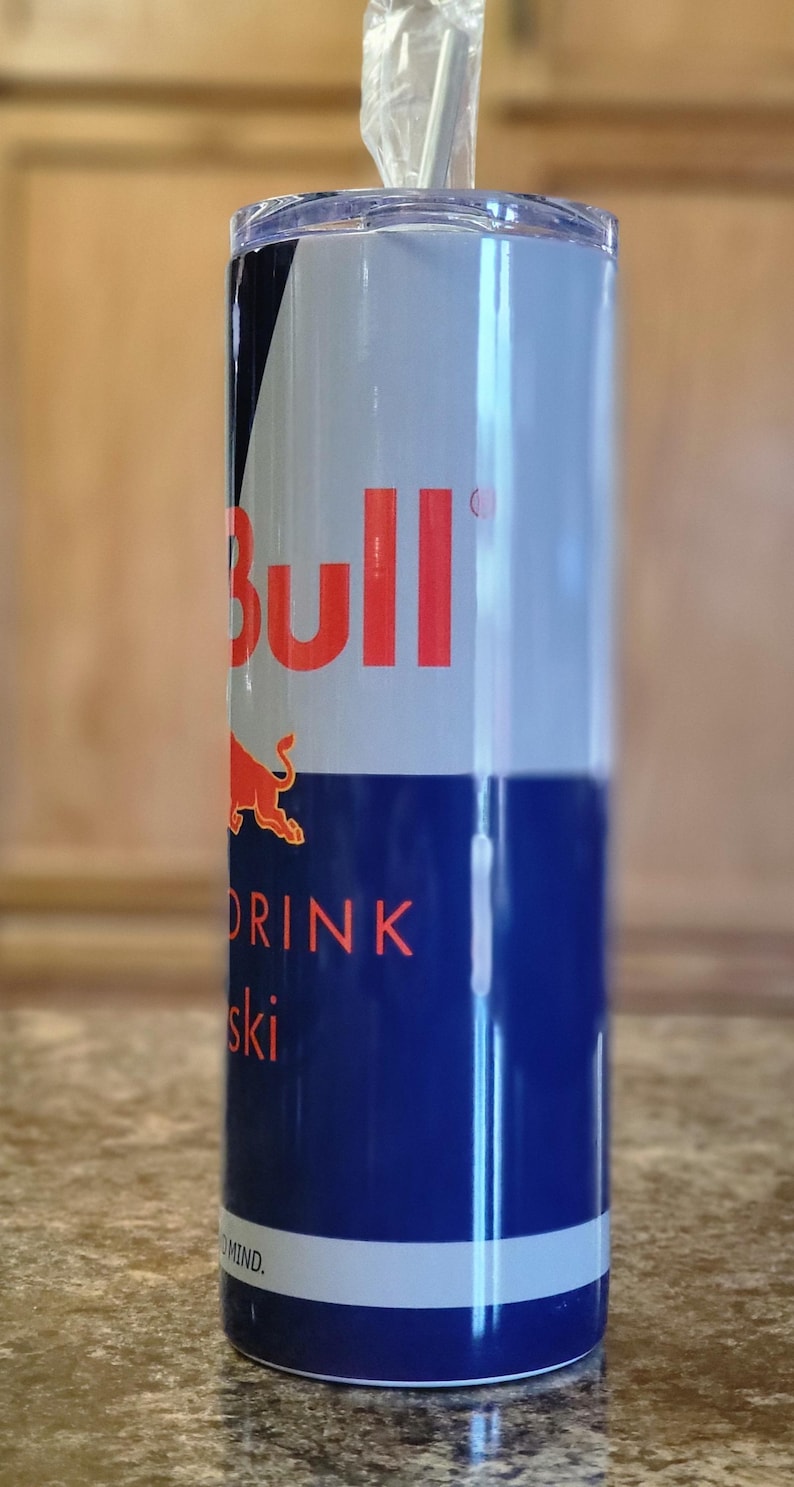 Pu&ograve; includere: Un bicchiere in acciaio inossidabile con un design Red Bull blu e bianco. Il bicchiere ha un coperchio trasparente e una cannuccia. Il testo sul bicchiere recita "Red Bull" e "Drink Your Wings".
