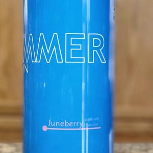 Może przedstawiać: Niebieski kubek termiczny ze stali nierdzewnej z napisem "SUMMER" w białym kolorze. Kubek ma r&oacute;żową kropkę i napis "Juneberry sztucznie aromatyzowany" w białym kolorze. Na dole kubka znajduje się napis "ENERGY DRINK Witalizuje ciało i umysł" w białym kolorze.