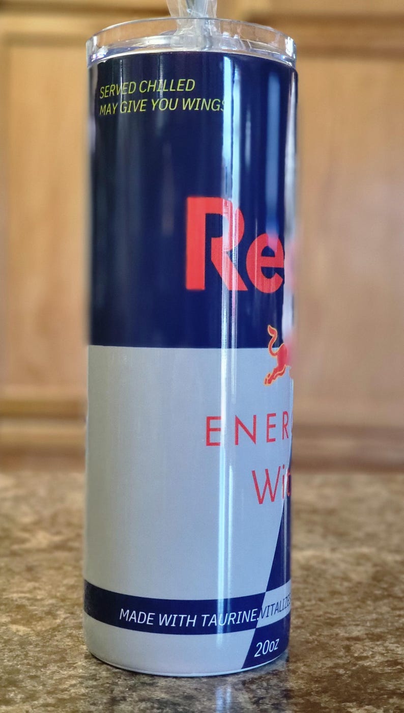 Pu&ograve; includere: Un bicchiere in acciaio inossidabile blu e bianco con un logo Red Bull e il testo "Servito freddo, pu&ograve; darti le ali". Il bicchiere ha anche il testo "Bevanda energetica" e "Prodotto con taurina, vitalizzato con zucchero".