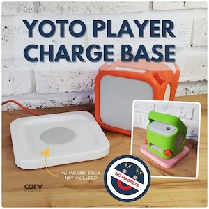 Op de afbeelding: Witte vierkante oplaadbasis met een grijs midden, oranje en witte Yoto Player en een groene en roze luidspreker. De tekst "YOTO PLAYER CHARGE BASE" staat bovenaan. De oplaadbasis is niet inbegrepen.