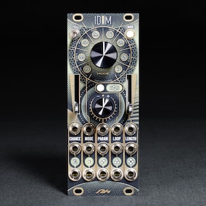 Puede incluir: Un módulo Eurorack negro y dorado con el texto "IDM" impreso en la parte delantera. El módulo tiene un botón grande en el centro y varios botones y botones más pequeños alrededor. El módulo está diseñado para crear música electrónica.