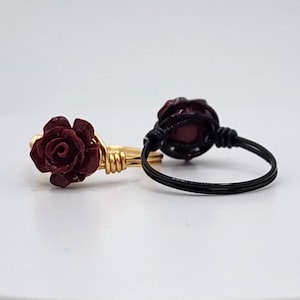 May include: Two rings with a burgundy rose design. One ring is gold wire wrapped around the rose, the other is black wire wrapped around the rose.