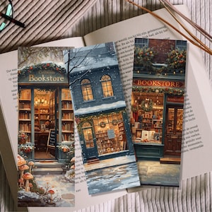 May include: Three decorative bookmarks featuring winter scenes of cozy bookstores. Each bookmark showcases a different bookstore facade, with snow-covered roofs, warm interior lights, and the word "Bookstore" displayed prominently.