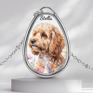 May include: Silver-toned pendant necklace featuring a watercolor portrait of a Cockapoo dog. The dog's name, "Stella," is written above the portrait. The pendant is teardrop-shaped and hangs from a delicate chain.