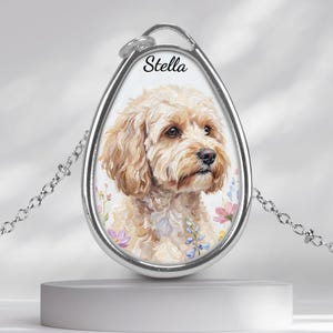 May include: Silver-toned pendant necklace featuring a watercolor portrait of a dog with the name "Stella" above the image. The dog has light brown fur and is surrounded by floral accents. The pendant hangs from a delicate chain.