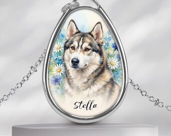 Könnte beinhalten: Eine silberfarbene ovale Anhängerkette mit einer Aquarellillustration eines Huskys, umgeben von weißen und blauen Blumen. Unter dem Hund ist der Name Stella in schwarzer Schreibschrift auf den Anhänger gedruckt. Die Kette ist sehr fein.