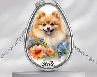 May include: Silver-toned pendant necklace featuring a watercolor portrait of a Pomeranian dog with a smiling expression. The dog is surrounded by colorful flowers, with the name "Stella" written below. The pendant hangs from a delicate chain.