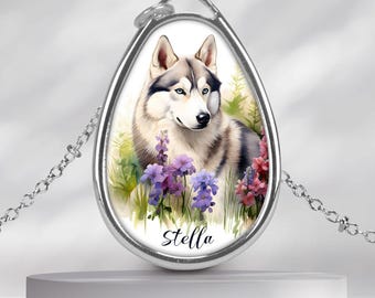 Könnte beinhalten: Eine silberfarbene ovale Anhängerkette mit einer gedruckten Illustration eines grau-weißen Huskys, umgeben von violetten und rosa Blumen. Der Name Stella ist in schwarzer Schreibschrift am unteren Rand des ovalen Einsatzes im Rahmen gedruckt.