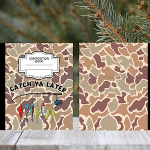 May include: Composition book with a camouflage pattern in shades of brown and tan. The cover features the text "Catch Ya Later" with fishing lures and a reel. The top has a white label that says "Composition Book".