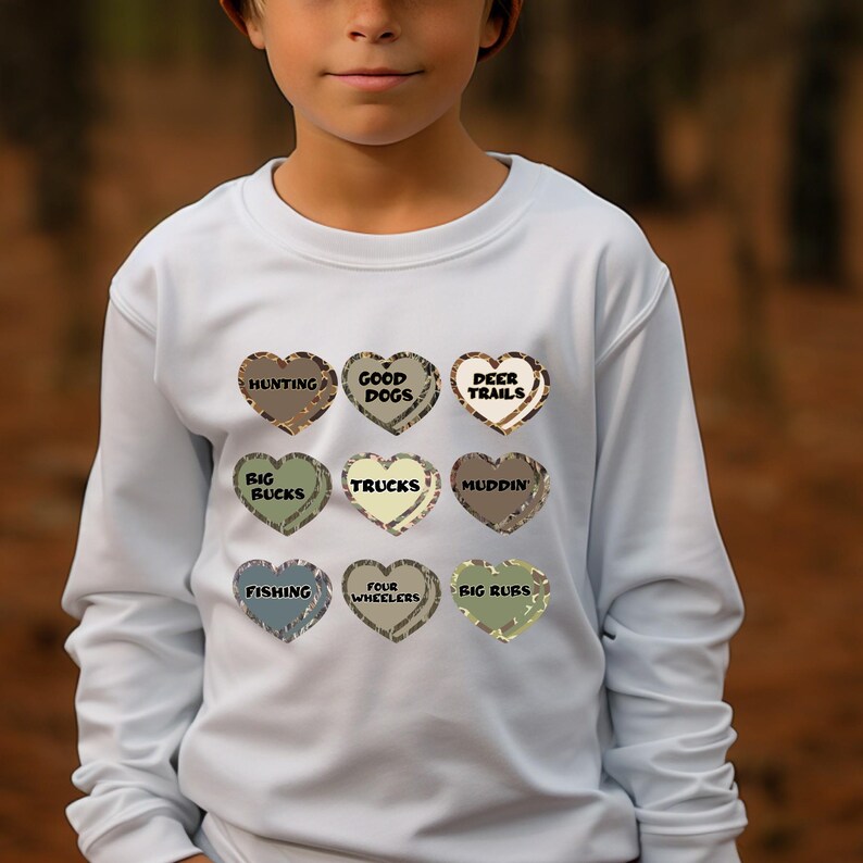 May include: Light blue long-sleeved sweatshirt with a camouflage pattern of nine hearts, each with a different phrase inside. The phrases are "Hunting", "Good Dogs", "Deer Trails", "Big Bucks", "Trucks", "Muddin'" , "Fishing", "Four Wheelers", and "Big Ruts".