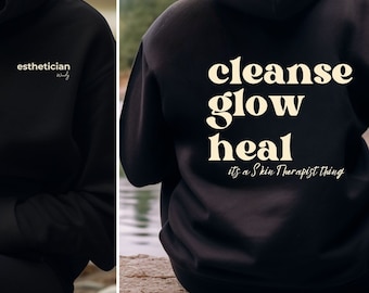 Op de afbeelding: Zwarte hoodie met de tekst "esthetician" op de voorkant en "cleanse glow heal it's a Skin Therapist thing" op de achterkant.