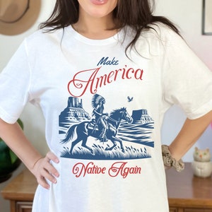 May include: White t-shirt with a blue and red graphic of a Native American riding a horse. The text "Make America Native Again" is printed on the shirt.