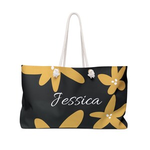 May include: A black tote bag with white rope handles and a yellow floral design. The bag has the name "Jessica" printed in white cursive lettering.