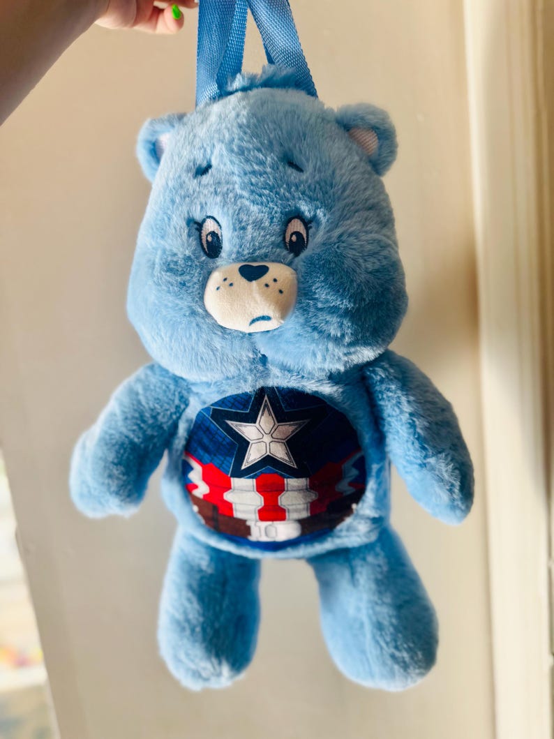Peut inclure: Un sac &agrave; dos en peluche bleu Care Bear avec un motif de bouclier Captain America sur le devant. Le sac &agrave; dos a une sangle bleue et une &eacute;toile blanche sur le bouclier.