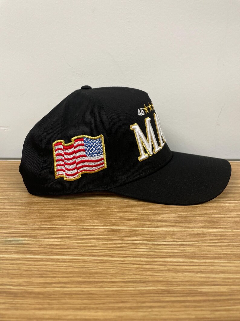 May include: A black baseball cap with a white embroidered American flag on the left side and the text "45**" and "MAKE" in gold embroidery on the right side.