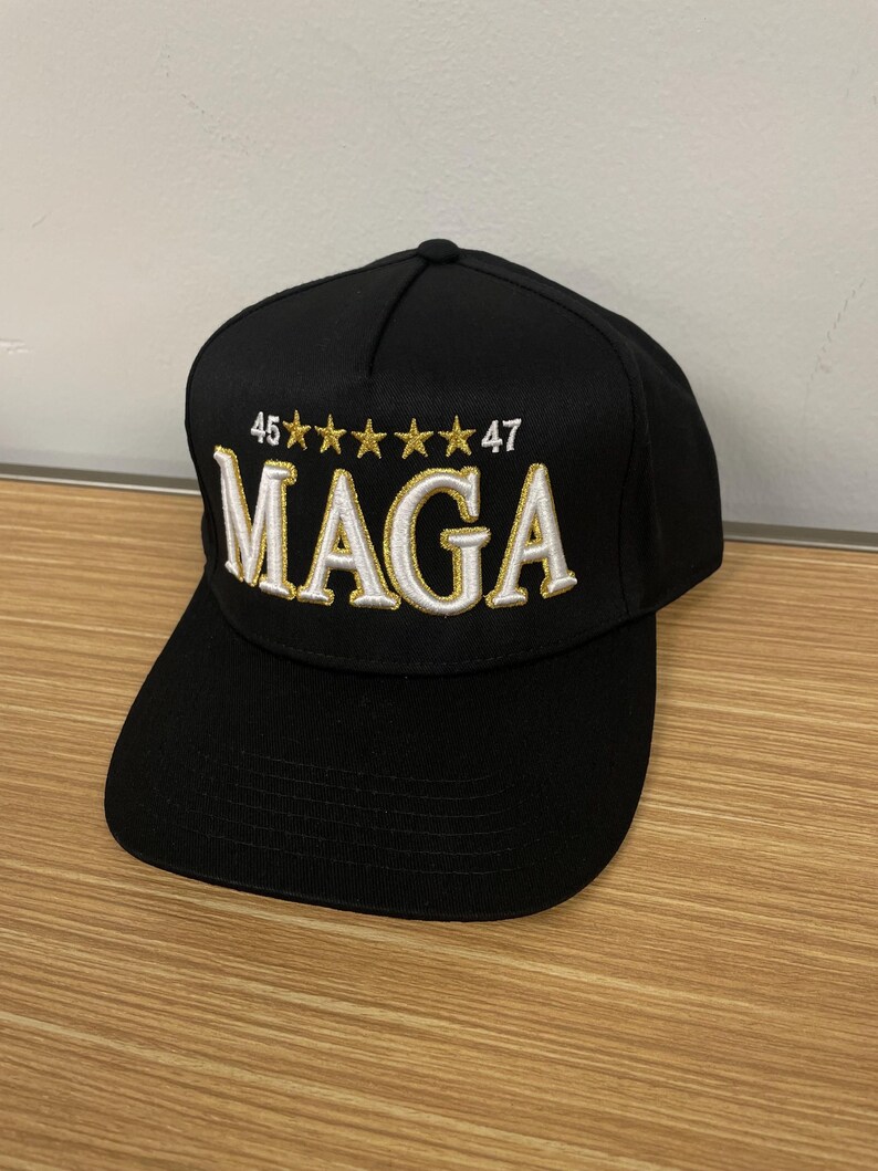 May include: A black baseball cap with a white embroidered "MAGA" logo and gold stars. The numbers "46" and "47" are also embroidered in gold.