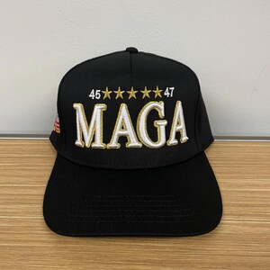 May include: Black baseball cap with white and gold embroidery that reads "45*****47 MAGA".