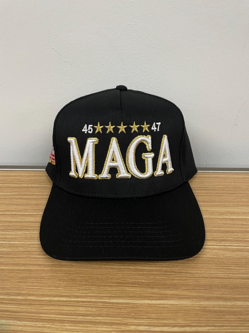 May include: Black baseball cap with white and gold embroidery that reads "45*****47 MAGA".