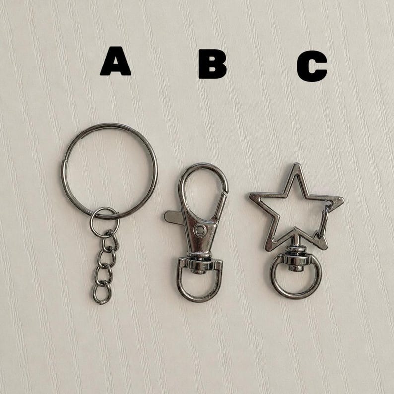 May include: Three silver-toned metal keychain components labeled A, B, and C. Component A is a circular split ring with a short chain. Component B is a lobster claw clasp with a swivel base. Component C is a star-shaped clasp with a swivel ring.
