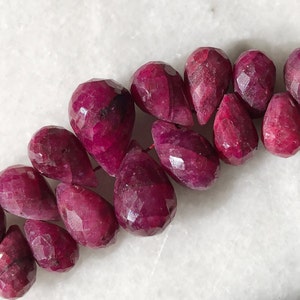 Op de afbeelding: Een streng facetgeslepen robijn kralen in een druppelvorm. De kralen zijn diep rood van kleur en hebben een gepolijste afwerking.
