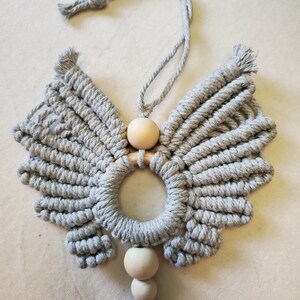 Peut inclure: Une suspension murale en macramé gris en forme d'aile d'ange avec un anneau en bois et trois perles en bois.