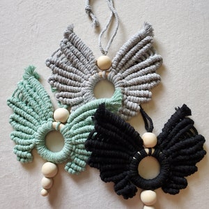 K&ouml;nnte beinhalten: Drei Makramee-Schmetterlings-Wandbeh&auml;nge mit Holzperlen. Die Schmetterlinge sind in Grau, Gr&uuml;n und Schwarz.