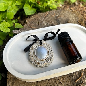 May include: A white ceramic tray with a silver and gold decorative ornament and a small brown glass bottle with a black lid.
