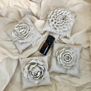 May include: Four grey fabric sachets with a flower design and a small brown glass bottle of essential oil.