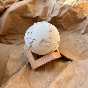 May include: A white plaster globe with a wooden stand. The globe is a representation of the Earth with continents and oceans.