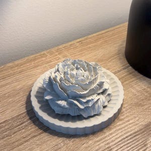 May include: A white ceramic flower shaped diffuser with a decorative, fluted base. The flower is detailed with realistic petals.