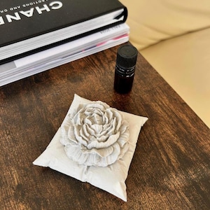 May include: A white ceramic flower cushion with a large, detailed flower design. The cushion is sitting on a dark brown wooden surface.