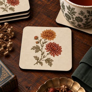Könnte beinhalten: Ein quadratischer Untersetzer mit cremefarbener Oberfläche, der eine botanische Illustration von zwei Chrysanthemen in Orange- und Dunkelrottönen mit grünen Blättern und Stielen zeigt, zentriert auf dem Untersetzer mit abgerundeten Ecken.