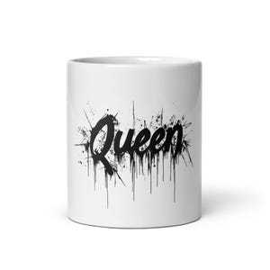 Puede incluir: Taza de cerámica blanca con un gráfico negro de la palabra "Queen" en un estilo de pintura que gotea.