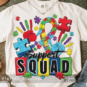 Op de afbeelding: Crèmekleurig T-shirt met een kleurrijk ontwerp met puzzelstukjes, handafdrukken en een lint. De woorden "Support Squad" worden in vette letters weergegeven. De zin "digitale download" is ook zichtbaar.