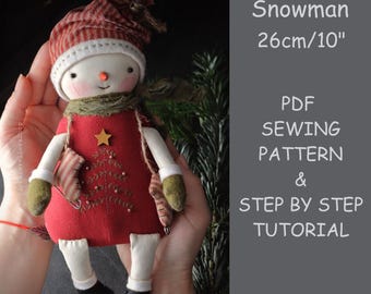 May include: A handmade snowman doll, approximately 10 inches tall, with a red dress, striped hat, and green scarf. The doll has a carrot nose, a stitched mouth, and a star on the front. The image also includes text that says "Snowman" and "PDF Sewing Pattern & Step by Step Tutorial."