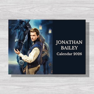 May include: A 2026 calendar featuring Jonathan Bailey. The image shows Bailey with a dark horse, wearing a vest and cream-colored shirt. The background has a blue and dark blue color scheme with lanterns.