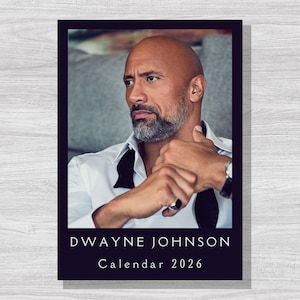 Può includere: Calendario 2026 con un ritratto di Dwayne Johnson. L'immagine mostra Johnson con una camicia bianca e un papillon nero. Il calendario ha un bordo blu scuro con il testo "Dwayne Johnson Calendar 2026" in bianco.