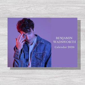 May include: A calendar featuring a person wearing a denim jacket, with the text "BENJAMIN WADSWORTH Calendar 2026" on a purple background. The image has a portrait orientation and is set against a light wood grain surface.