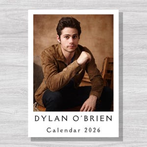 May include: A 2026 calendar featuring a portrait of Dylan O'Brien. The image shows O'Brien in a brown suede jacket and dark pants. The calendar has a white border with the name "DYLAN O'BRIEN" and "Calendar 2026" printed in black.