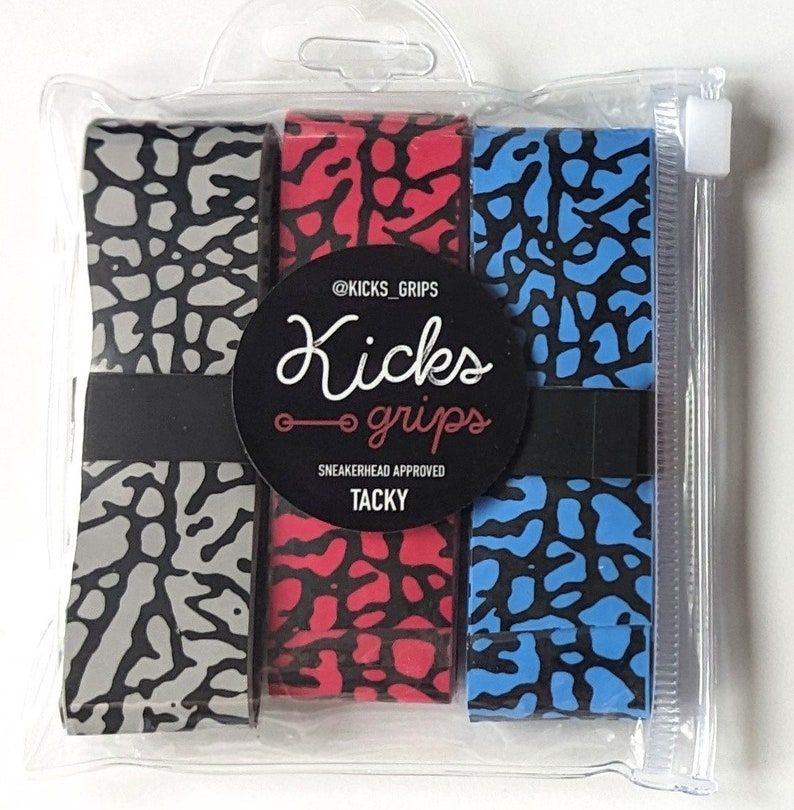 May include: Three rolls of adhesive grip tape in gray, red, and blue, each featuring a black elephant print pattern. The rolls are secured by a black band with a circular label reading @KICKS_GRIPS, Kicks grips, SNEAKERHEAD APPROVED, TACKY.