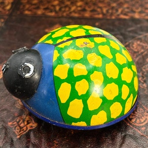 May include: A green and yellow ladybug toy with a black head and blue accents. The toy is made of metal and has a whimsical design.