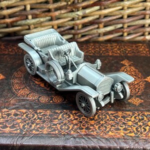 May include: A silver pewter model of a vintage car with a detailed interior and a 'Saxon' logo on the front.